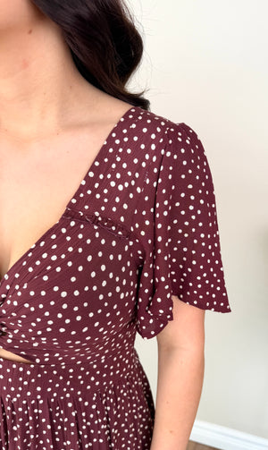 Close-up of a woman wearing a burgundy dress with white polka dots, featuring a wrap-style neckline and short flutter sleeves.
