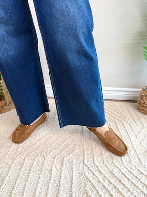 A person wearing blue wide-leg jeans and tan suede loafers standing on a textured cream rug indoors.